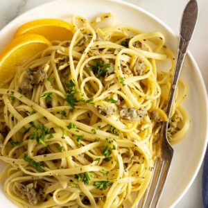 linguine with clam sauce on white plate with lemon wedges and fork