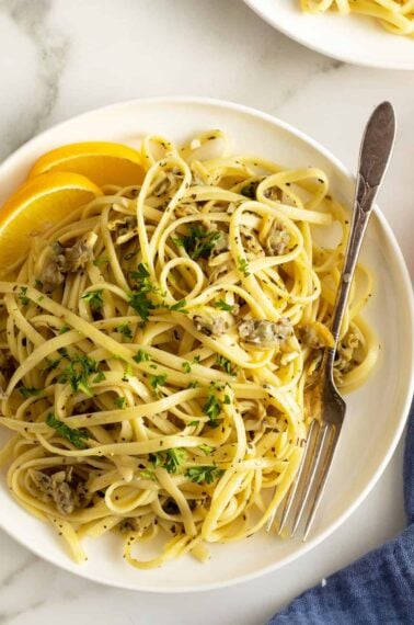 linguine with clam sauce on white plate with lemon wedges and fork