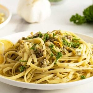 linguini with clam sauce on a white plate with a slice of lemon on the side