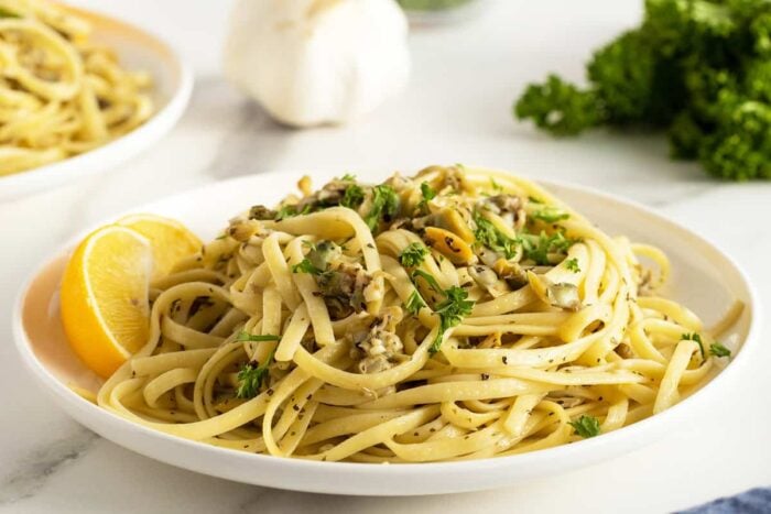 linguini with clam sauce on a white plate with a slice of lemon on the side