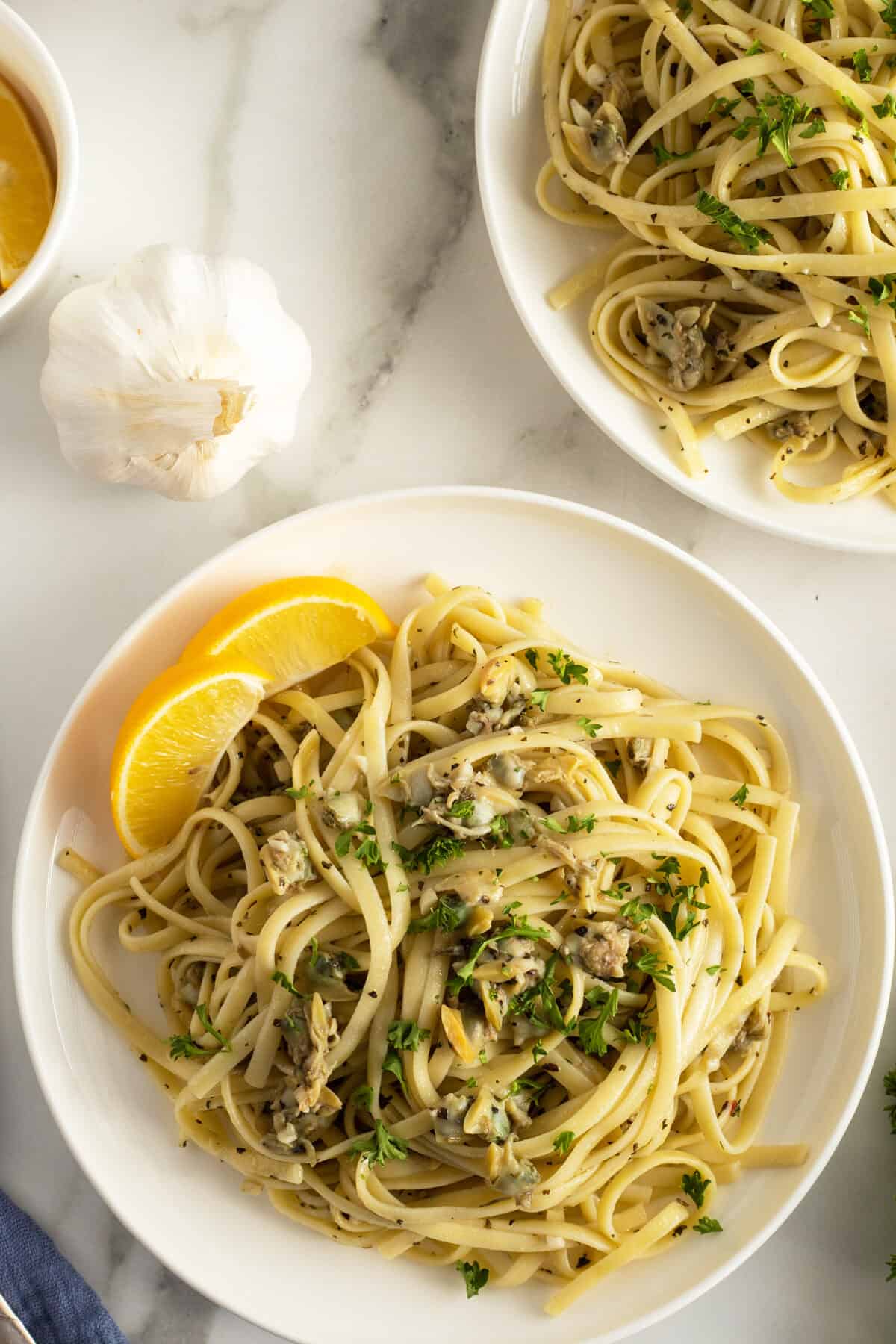 linguini with clam sauce on two white plates with lemon wedges