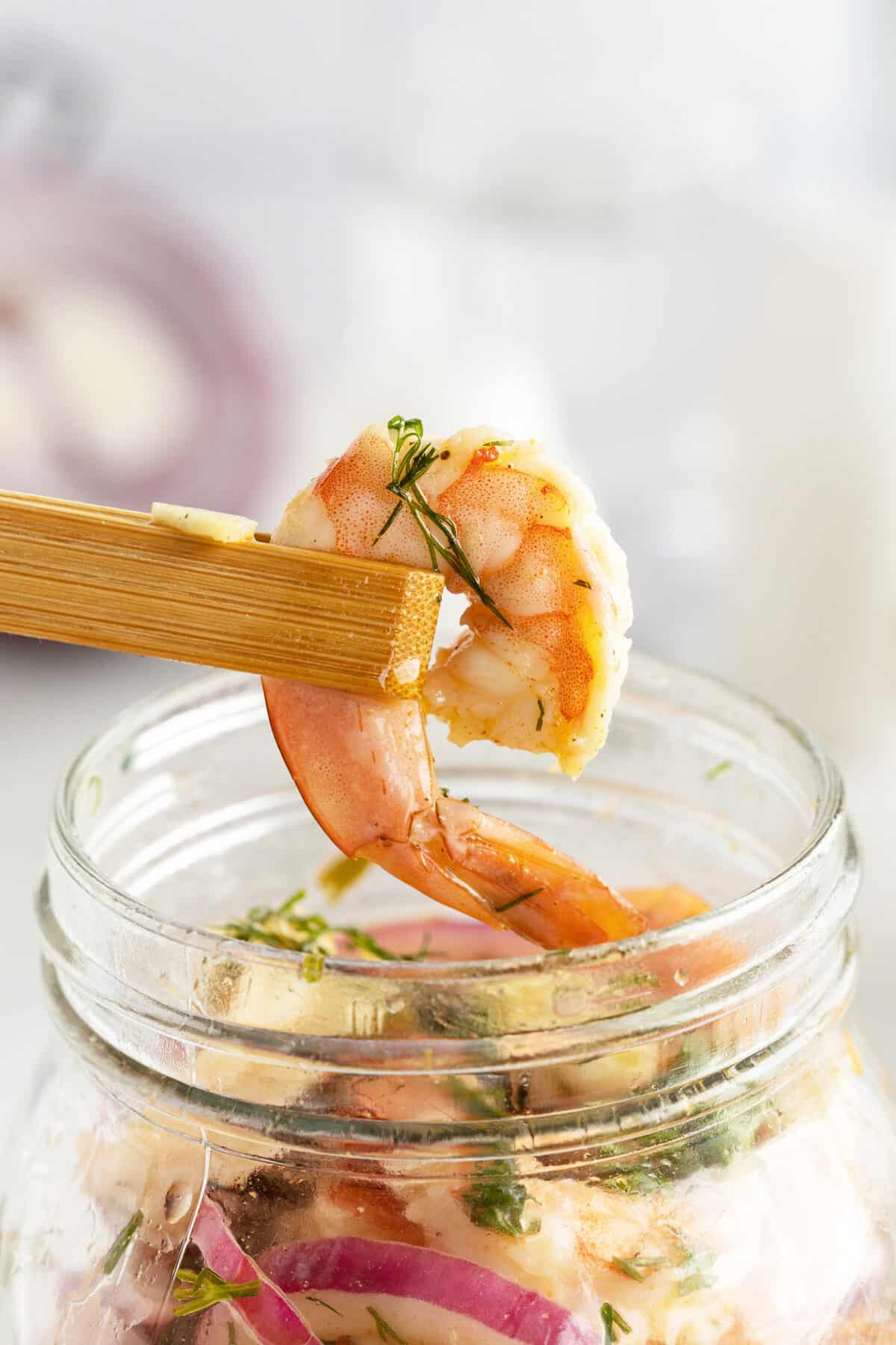 pickled shrimp being held up by wooden tongs