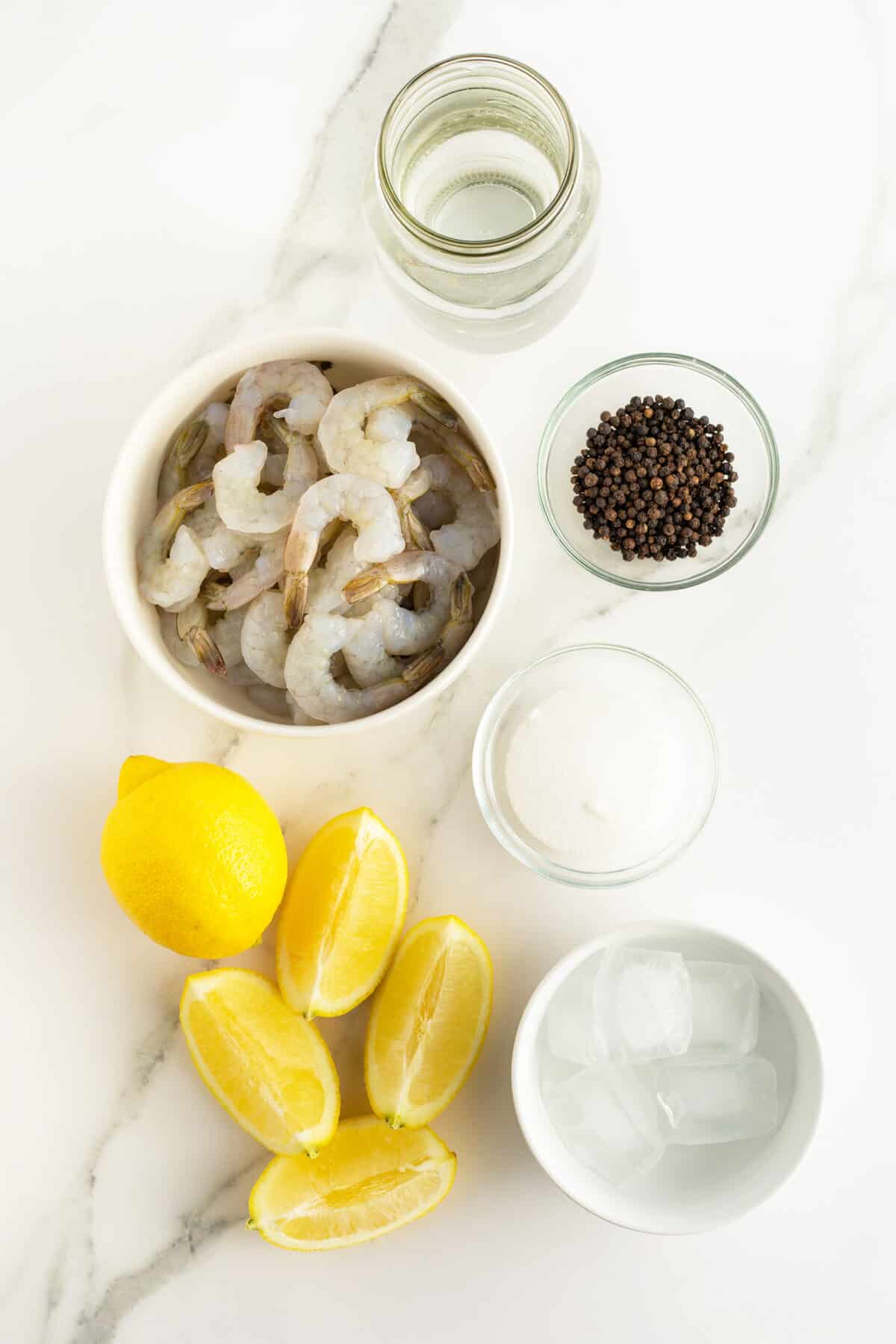 poached shrimp ingredients in small white bowls and sliced lemons