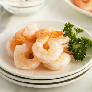 poached shrimp on a stack of white plates with parsley garnish