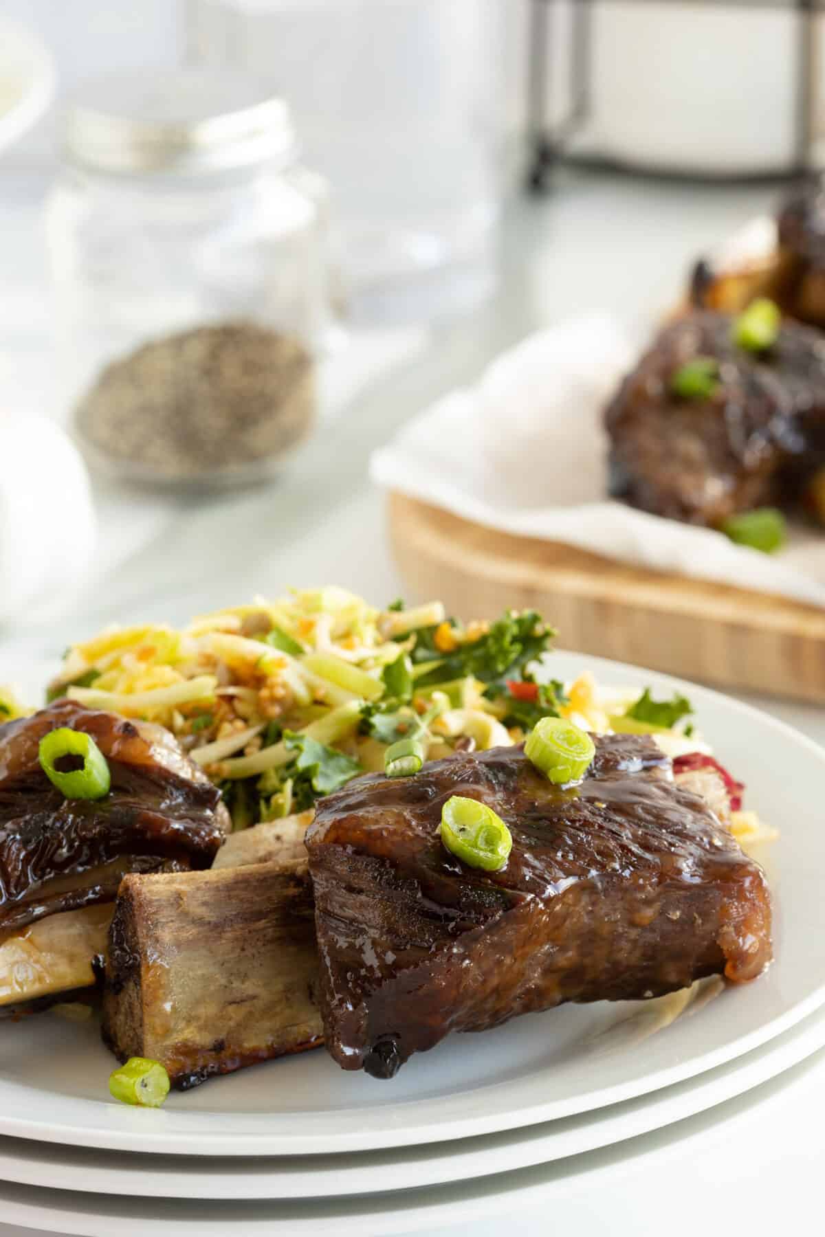 beer glazed beef ribs on a stack of white plates with green onion sprinkled on top