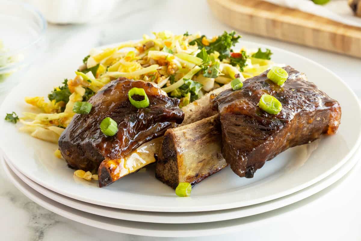 beer glazed beef ribs on a white plate with a salad
