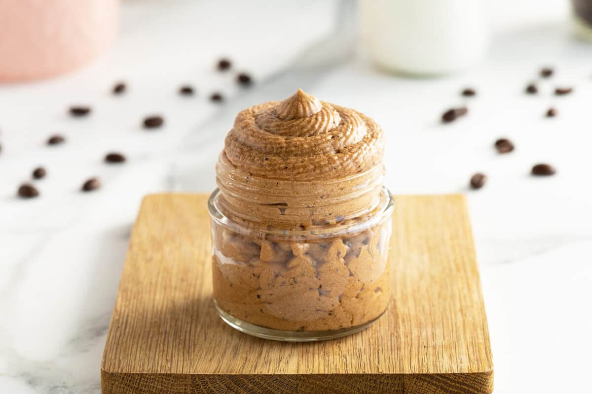Coffee buttercream icing in a small clear jar on a cutting board