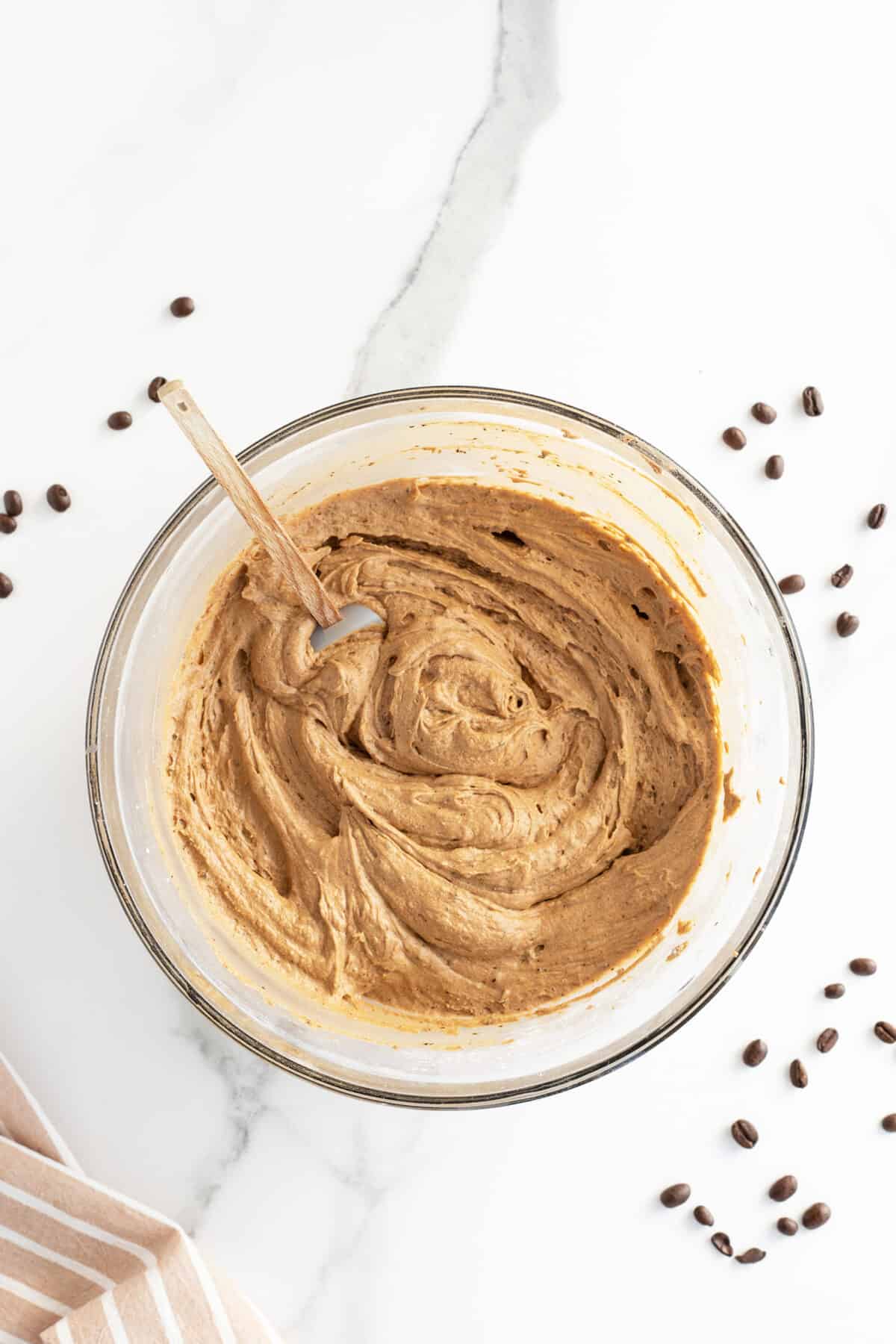 Coffee buttercream icing in a clear mixing bowl with a spatula