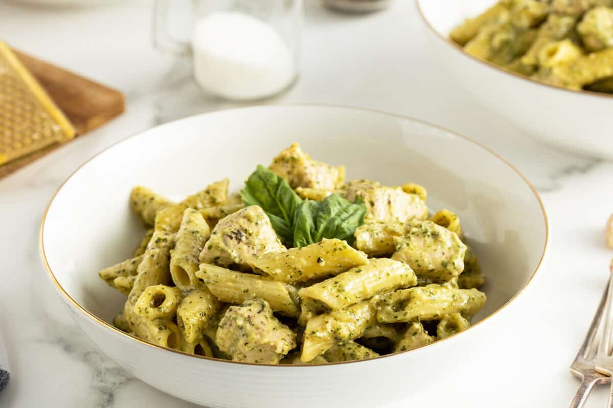 creamy chicken pesto pasta in a bowl with fresh basil leaves on top