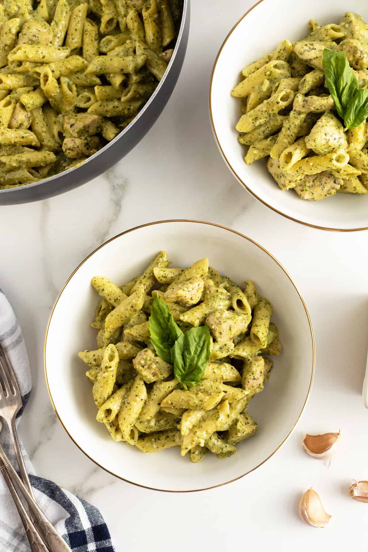 creamy chicken pesto pasta in two white bowls garnished with basil leaves