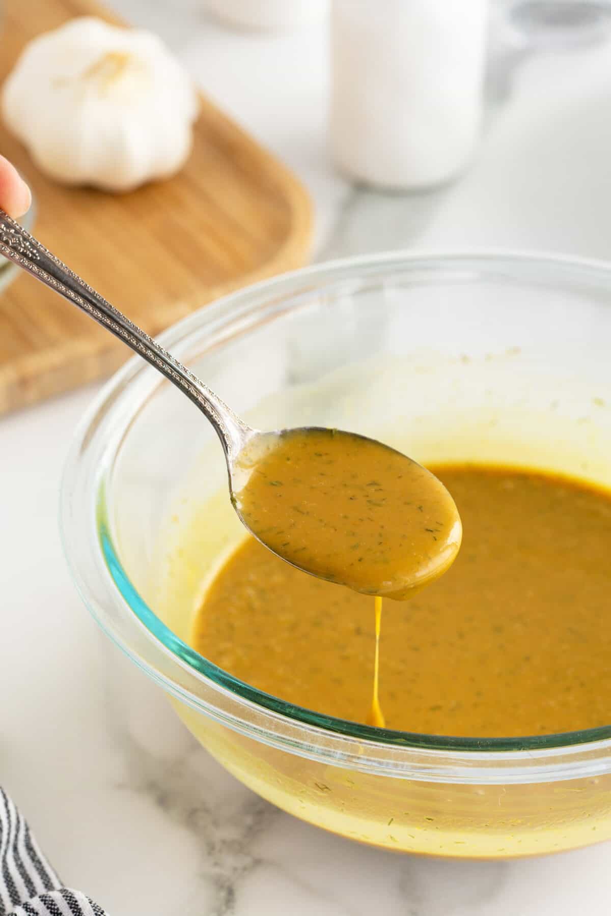 honey mustard dressing in a mixing bowl with a spoon dripping dressing