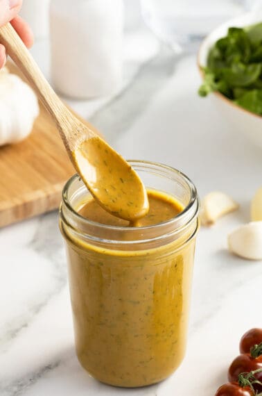 honey mustard dressing in a mason jar with a wooden spoon lifting out dressing