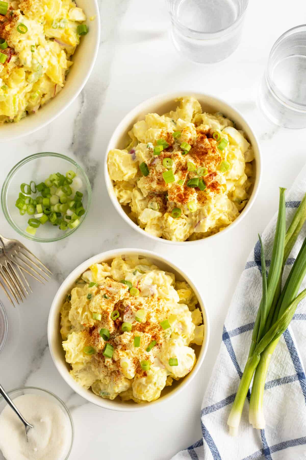 mom's potato salad in two large bowls with green onions on the side