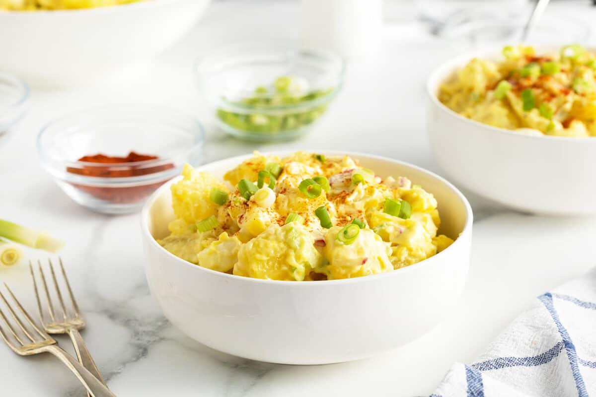 mom's potato salad in a large white bowl with sliced green onions on top