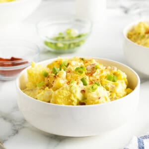 mom's potato salad in a large white bowl with sliced green onions on top