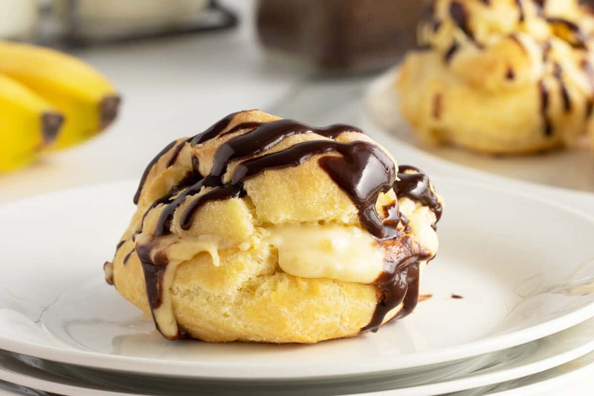 banana cream puff on a white plate with chocolate drizzle