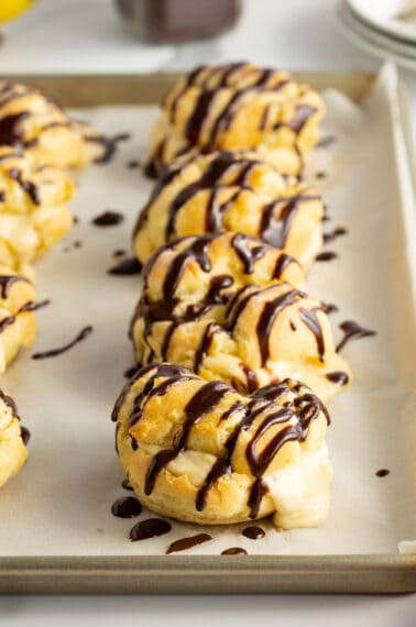 banana cream puffs lined up on a baking tray drizzled with chocolate