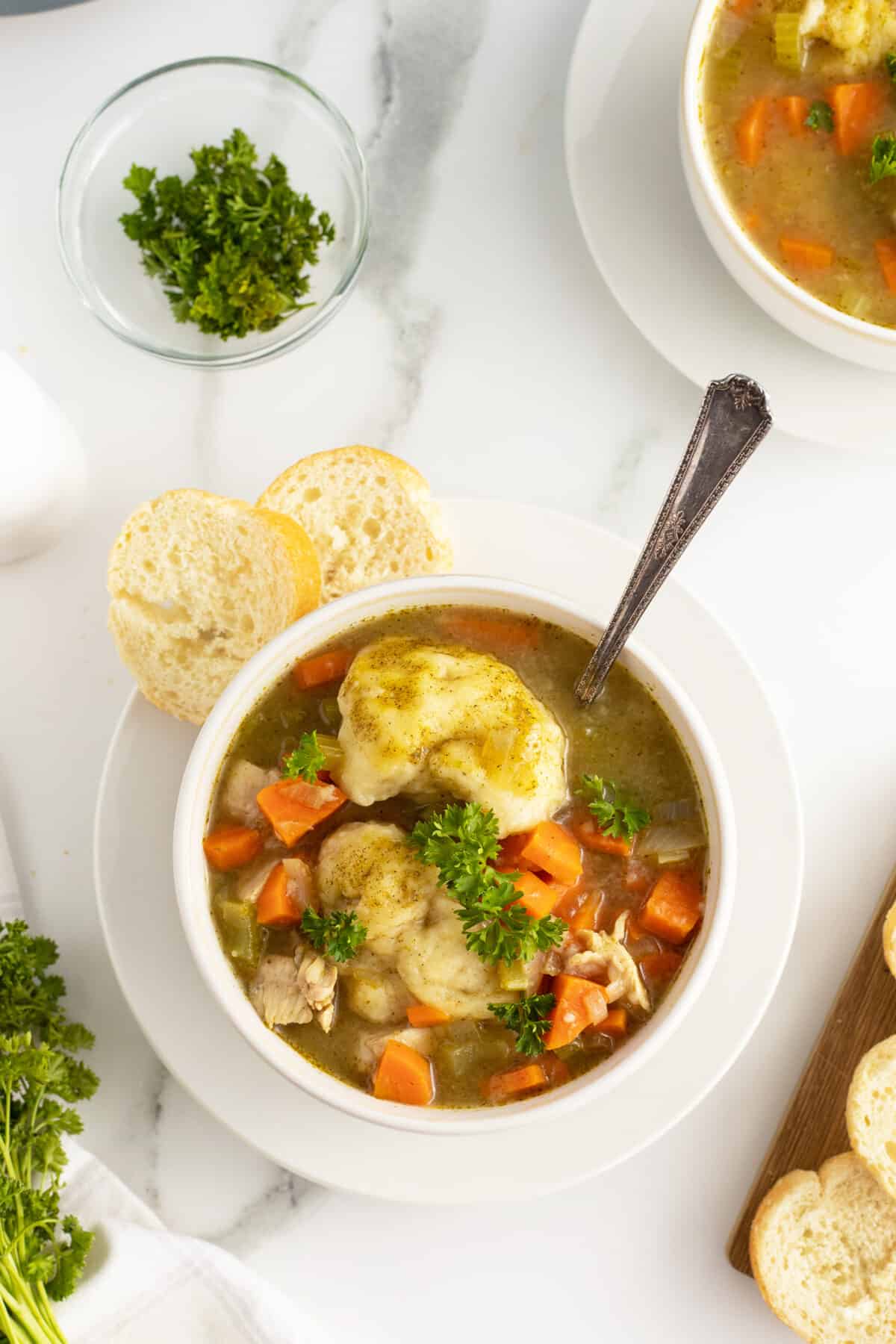 chicken and dumpling soup in a white bowl with sliced bread on the edge of the dish