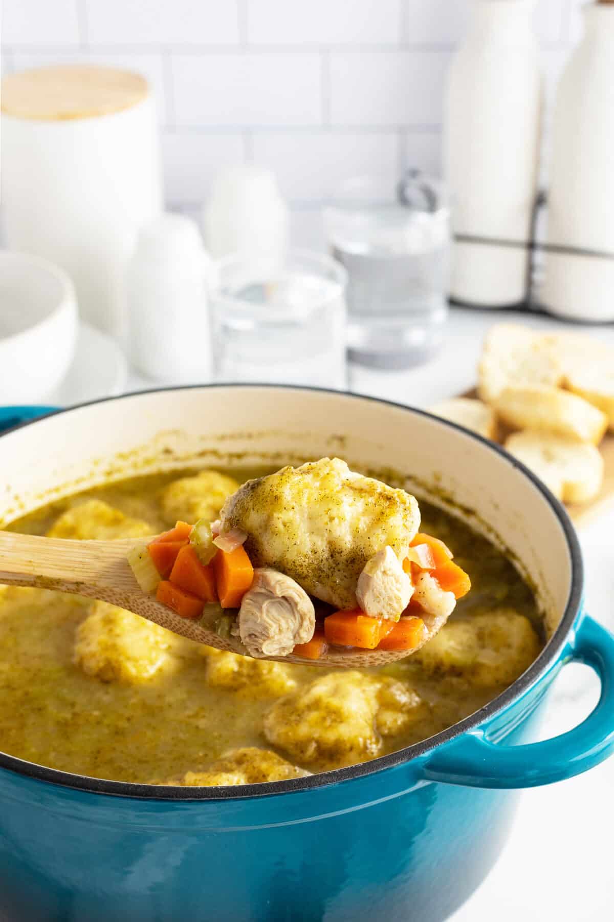 chicken and dumpling soup in a blue pot and a dumpling on a wooden spoon