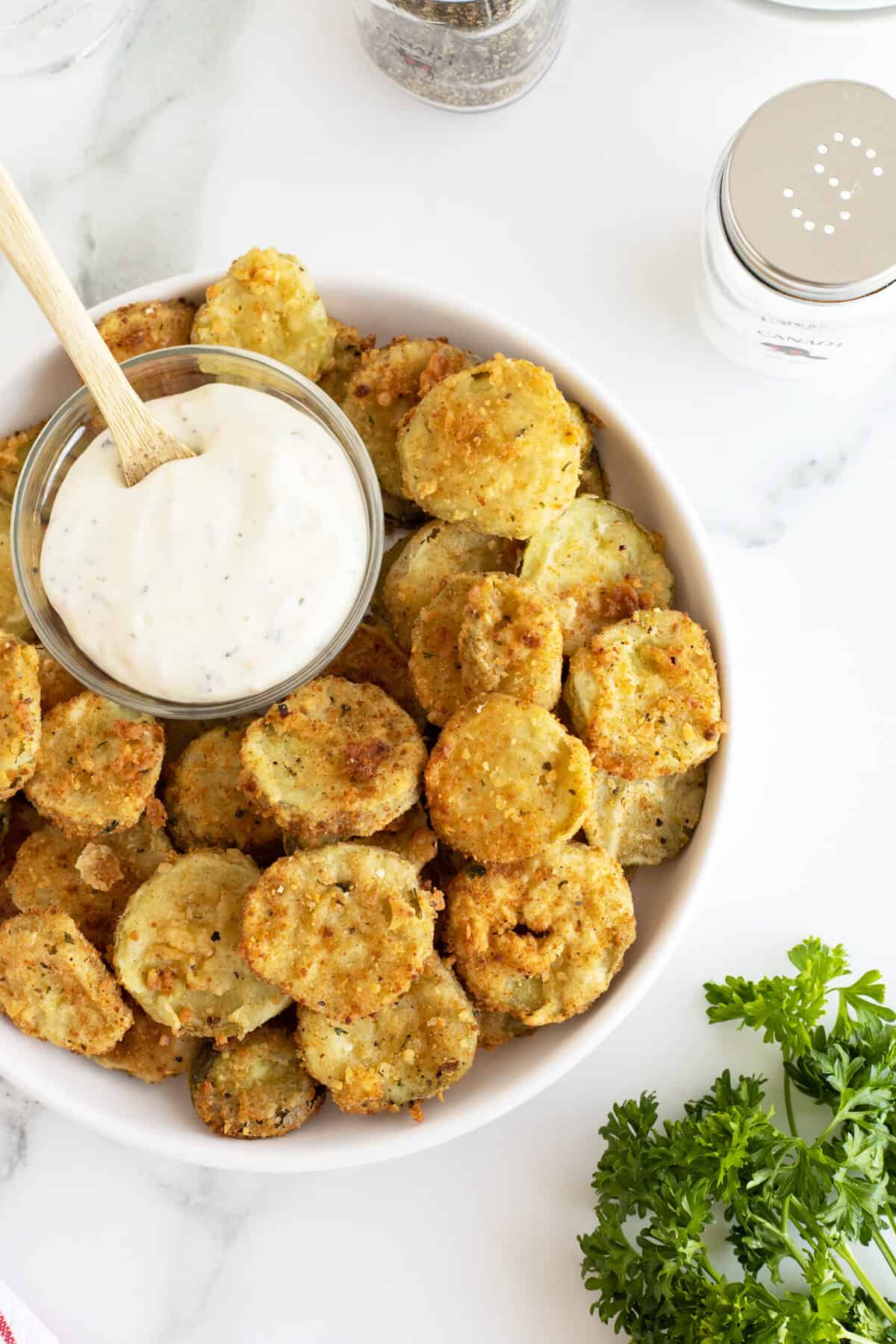 fried pickles on a plate with a clear bowl with dip