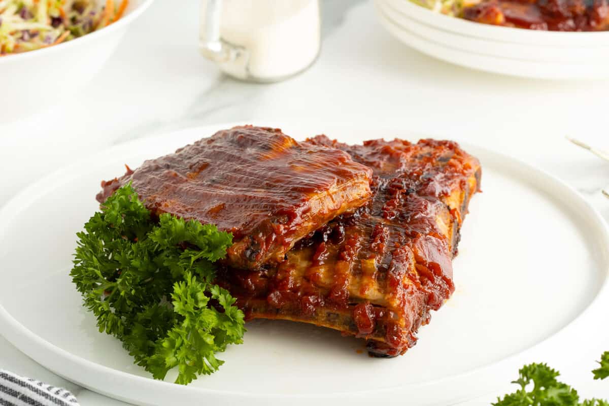 glazed spareribs on a plate with a big sprig of fresh parsley
