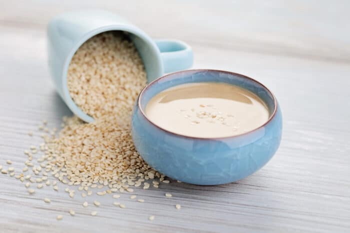blue bowl of tahini and a blue cup full of sesame seeds