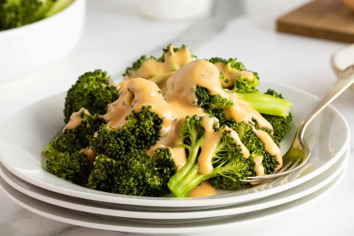 cheese sauce drizzled on cooked broccoli on a white plate