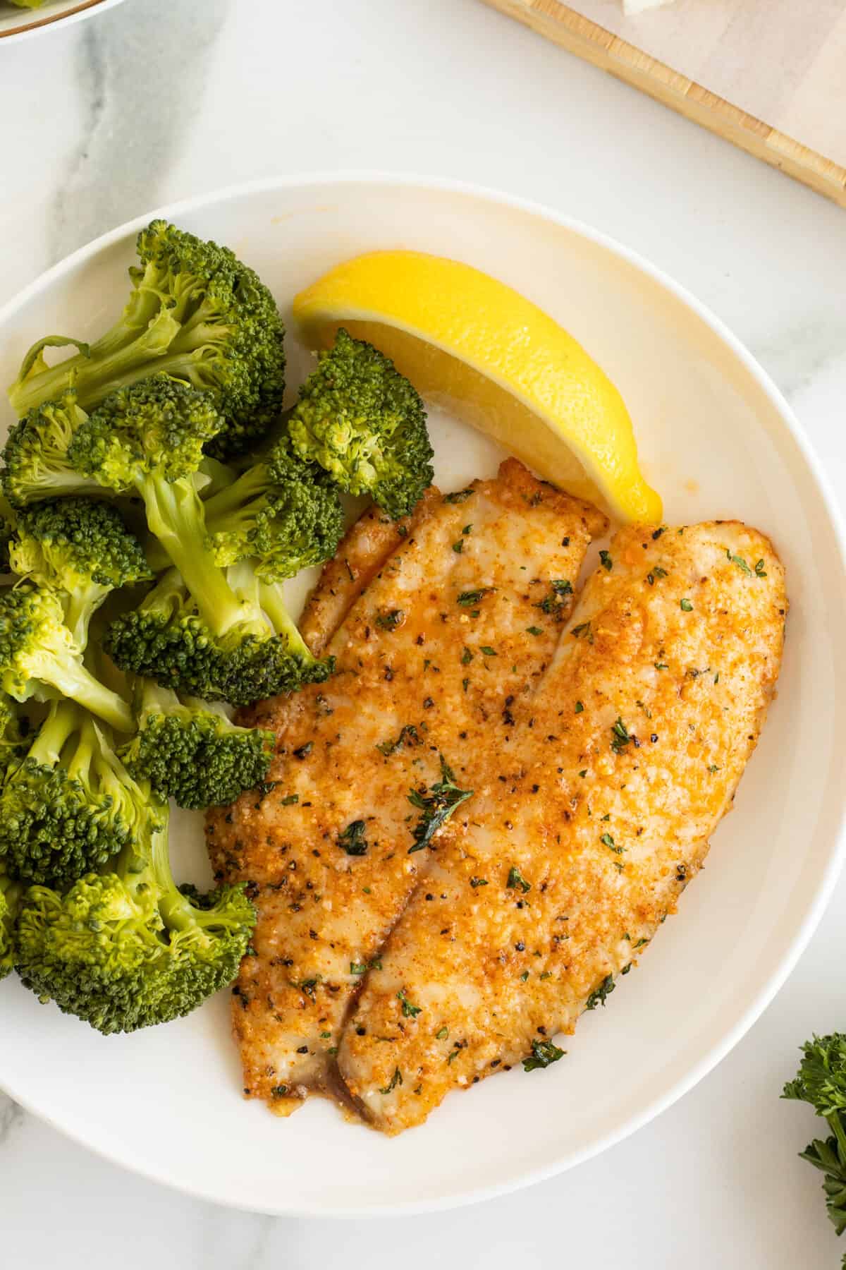 Parmesan crusted tilapia on a white plate with broccoli 