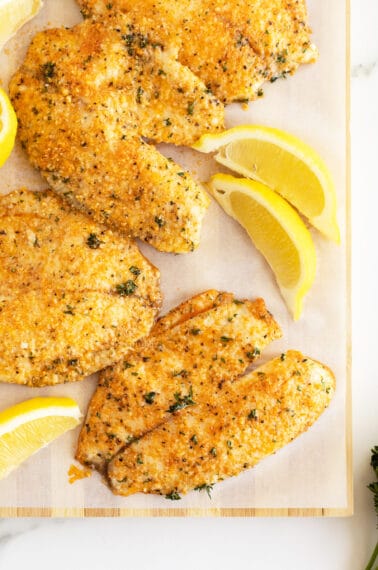 Parmesan crusted tilapia on a baking pan with slices of lemons