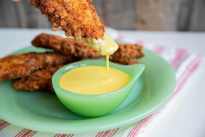 honey mustard sauce in a small green bowl with a chicken finger dipped in