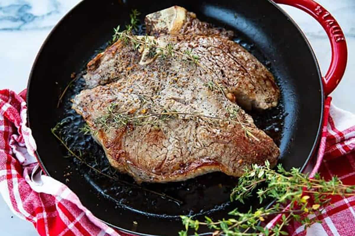 steak on a black plate with sprigs of fresh rosemary on top