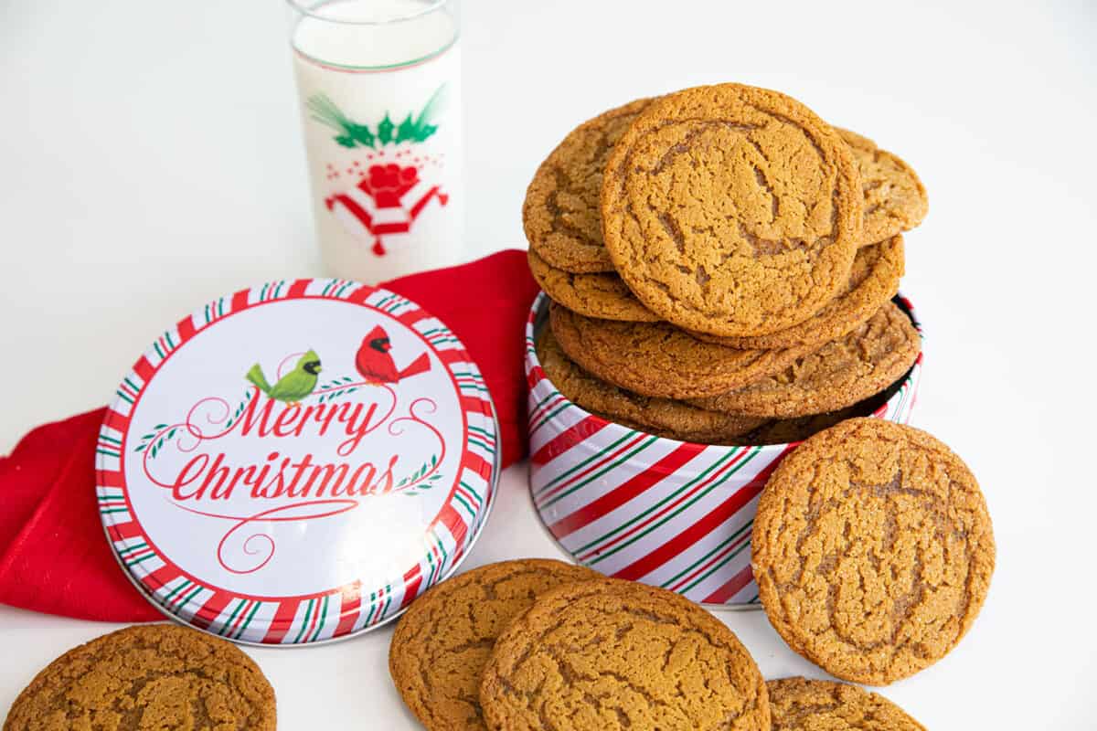 Spice cookies in a Christmas tin with a glass of milk.