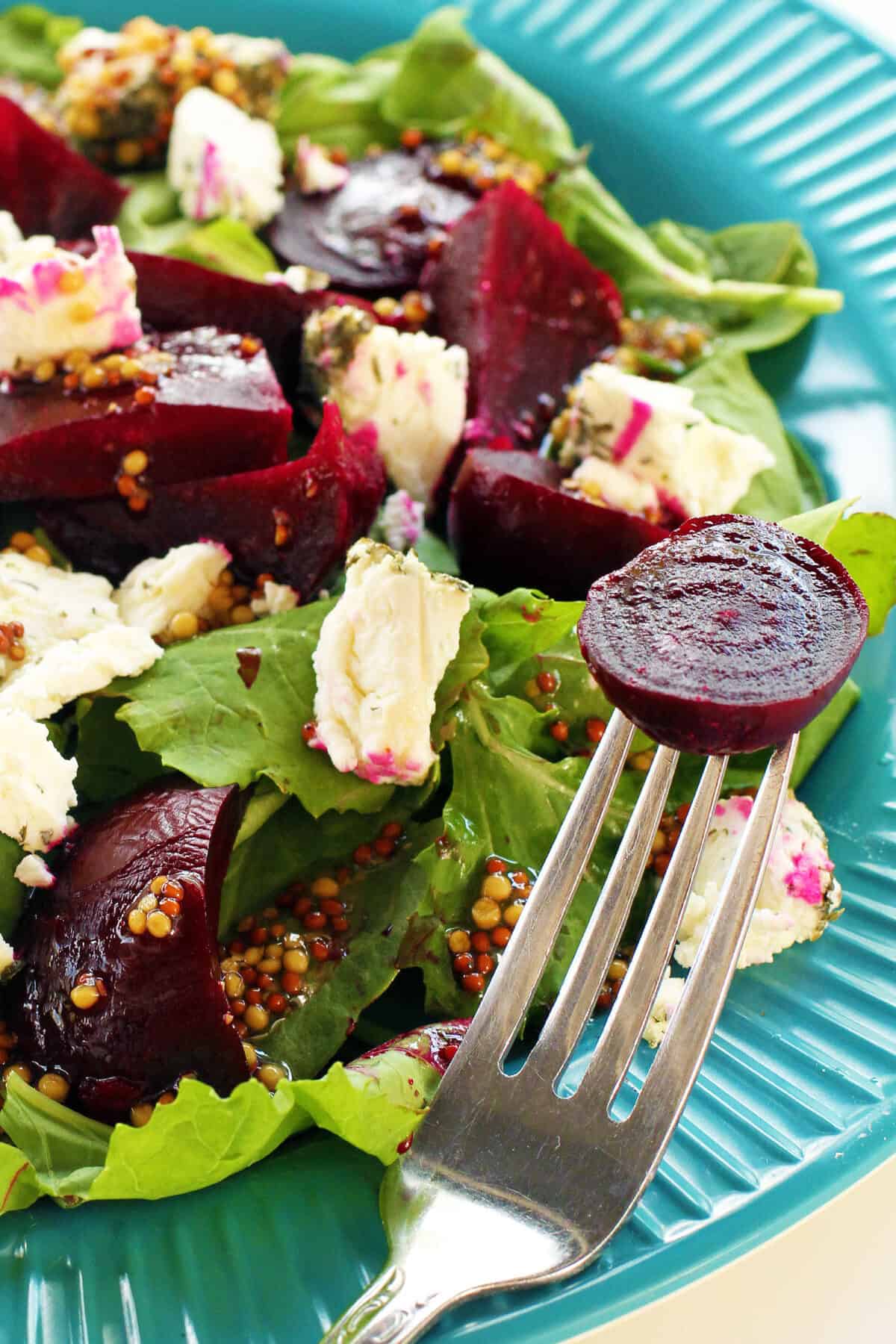 a roasted beet on a fork on a plate of beet salad