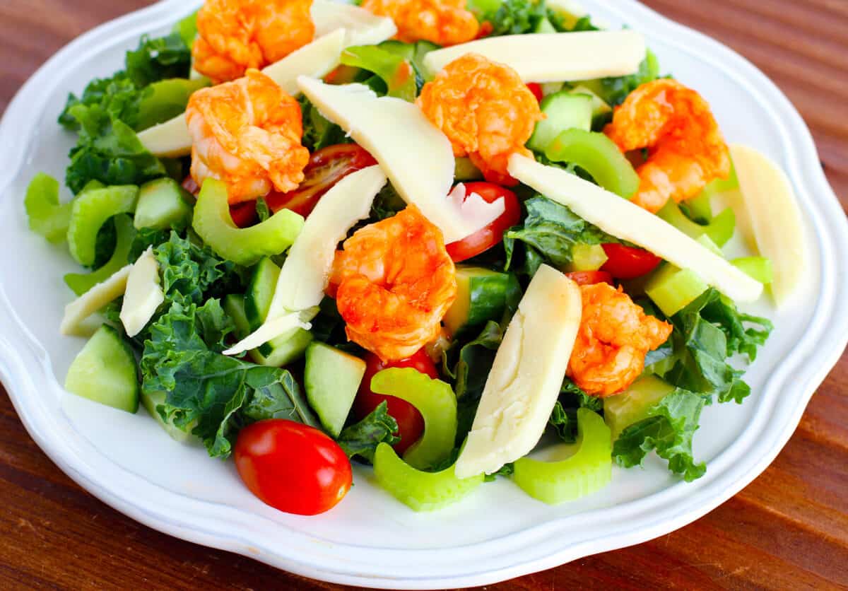 buffalo shrimp kale salad on a white plate photographed on a table
