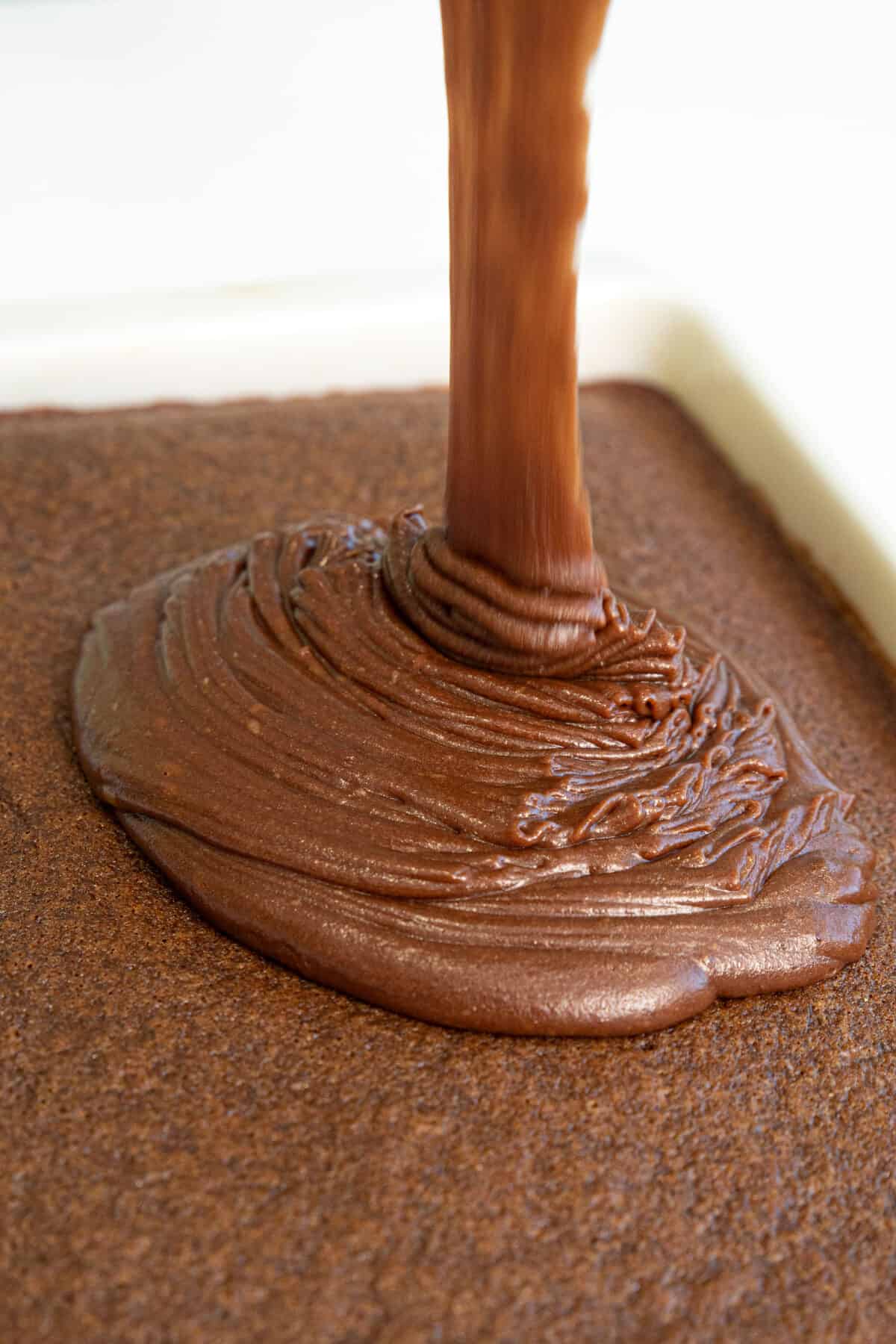 pouring hot fudge frosting onto a Texas sheet cake