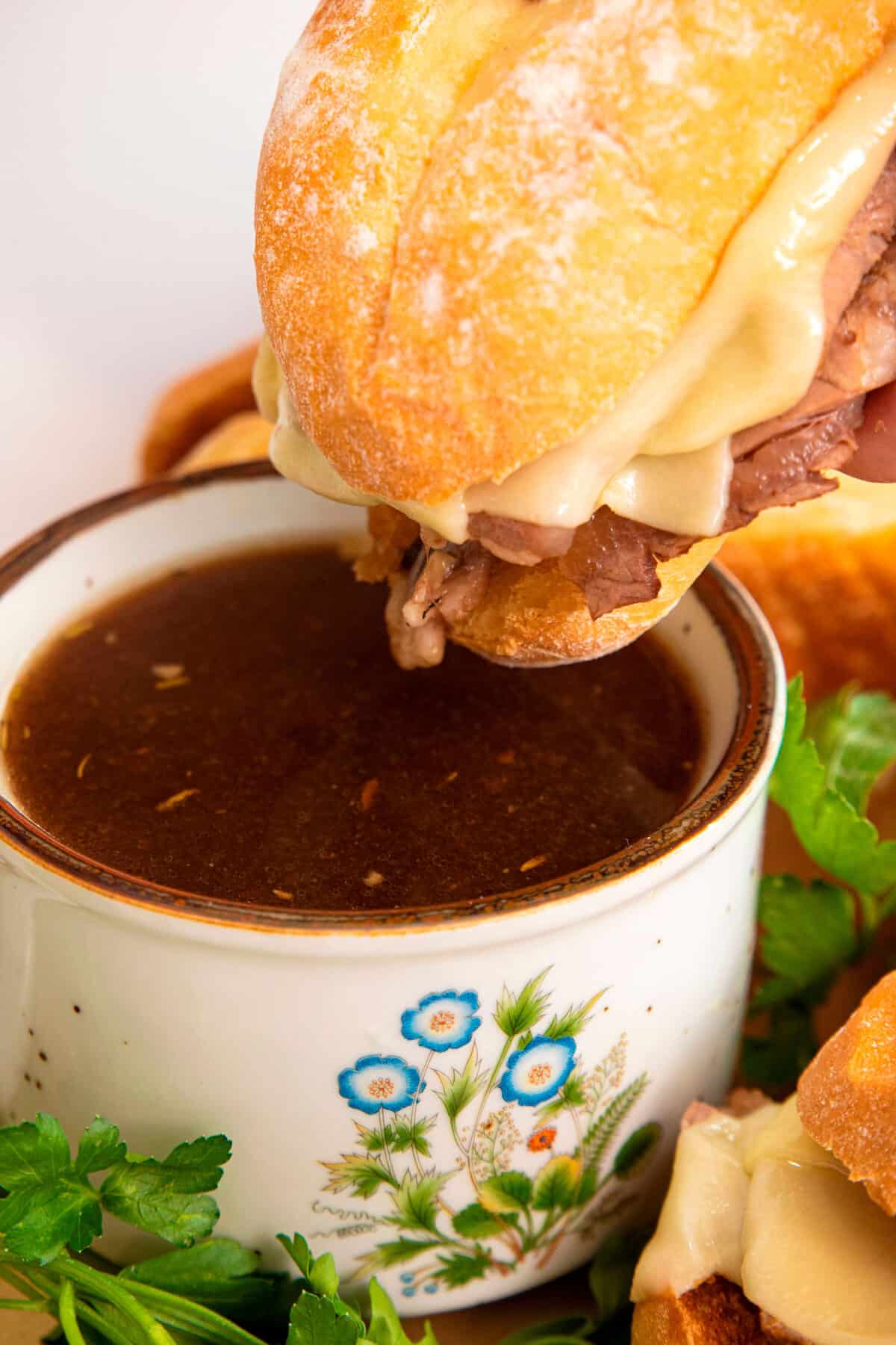 dipping a beef dip into au jus in a container
