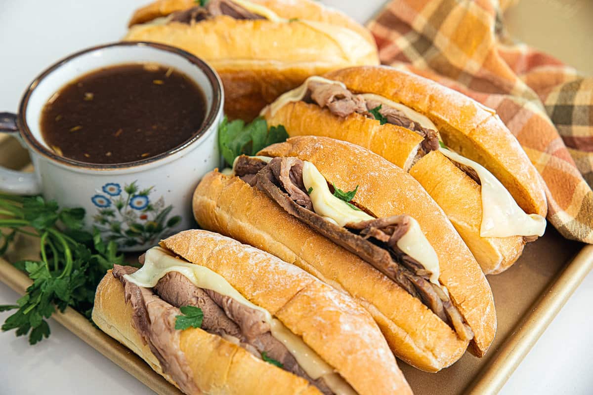prime rib beef dips and a bowl of au jus on a gold baking sheet