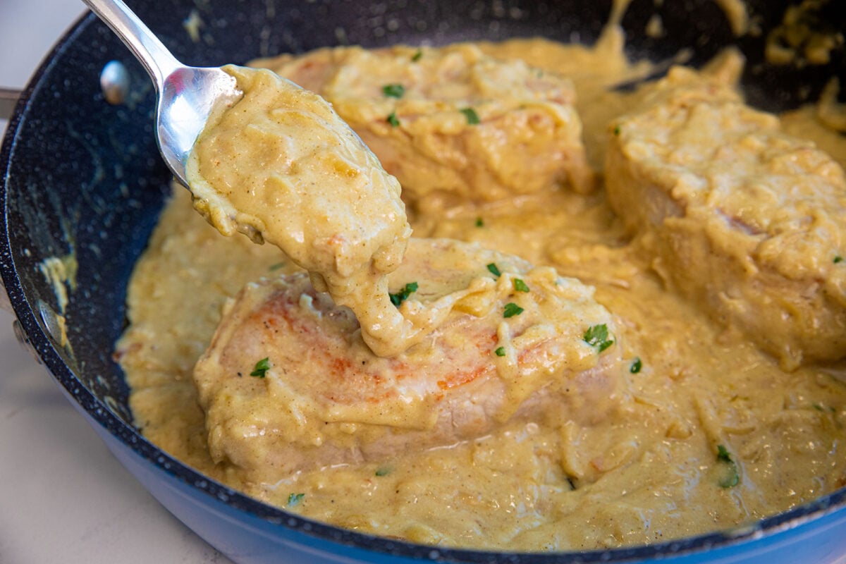 pork chops in a pan with sauce cooked and spooning sauce overtop