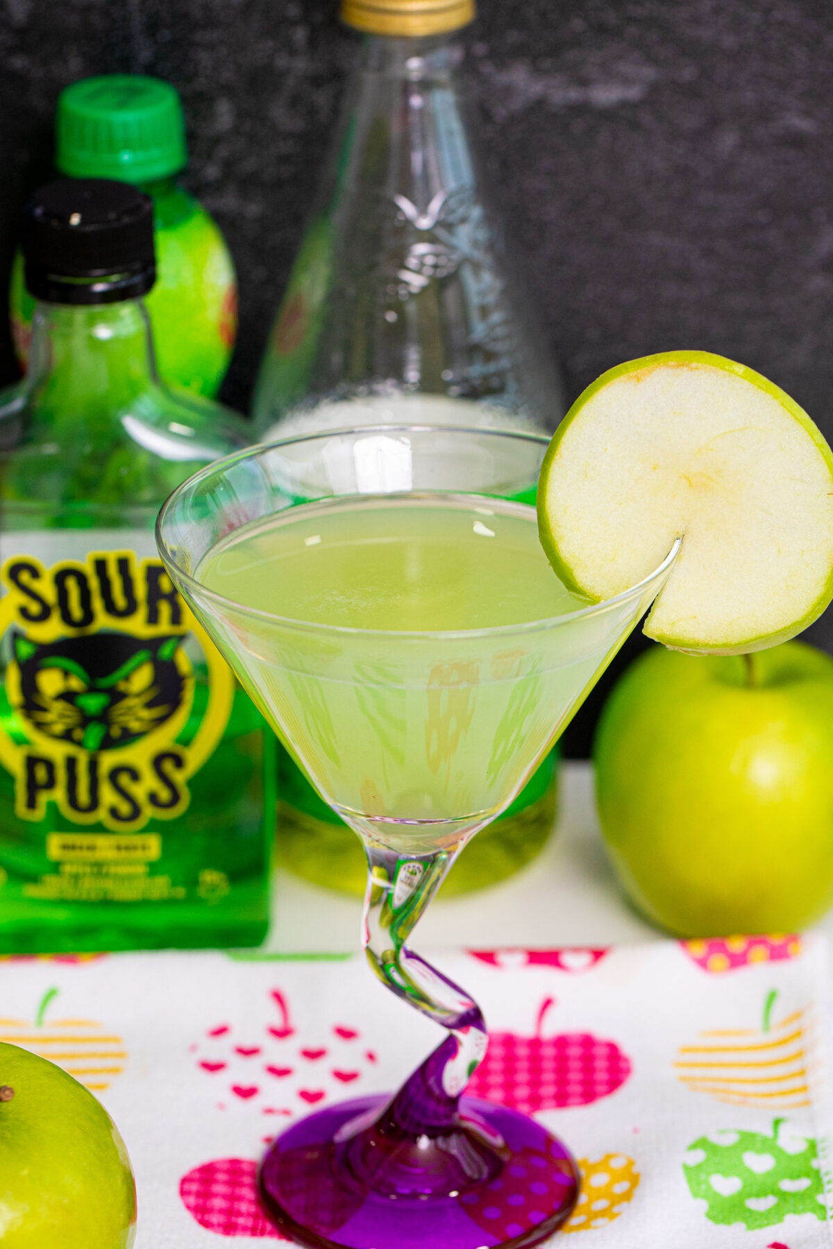 An Appletini close-up in a martini glass with green apple slice.