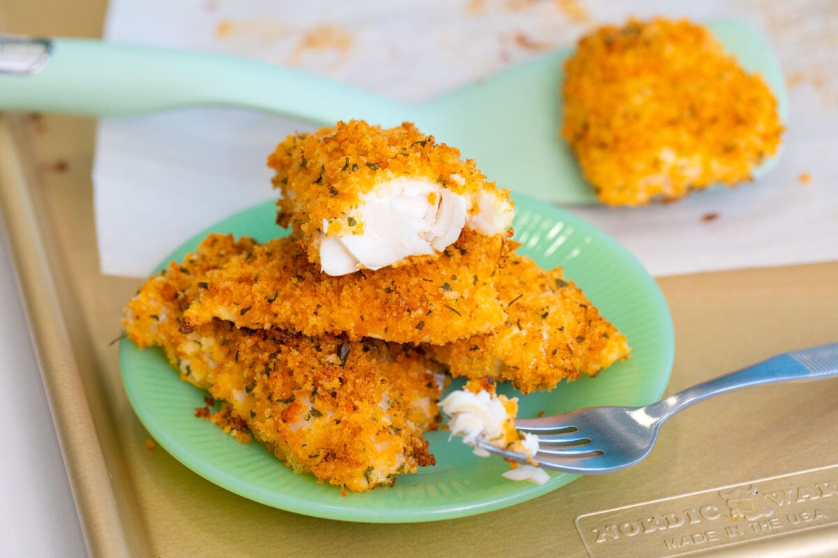 baked cod stacked on a green plate and a fork with flaky white cod fish.