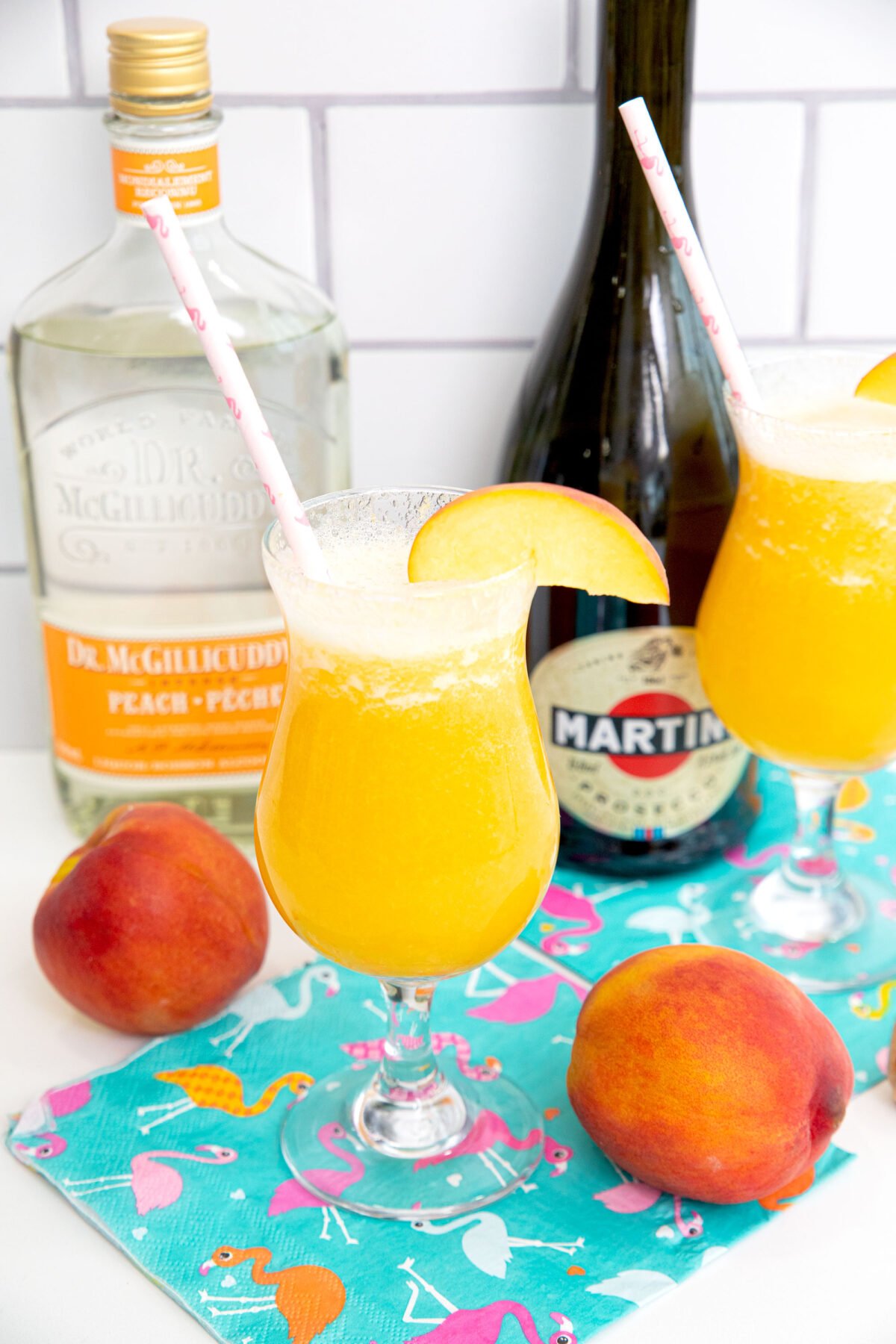 Two peach bellinis on a counter with peach schnapps and prosecco in the background.
