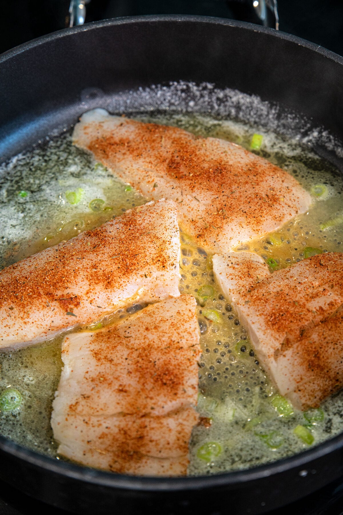 cod fillets with Cajun seasoning on top in a skillet cooking in butter