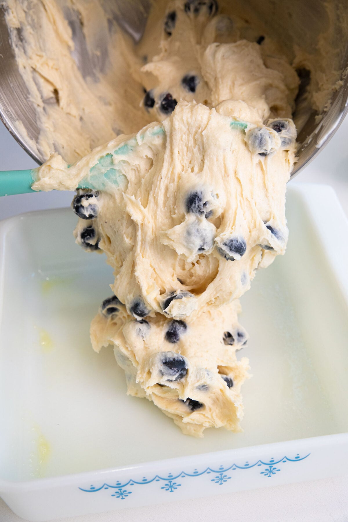 pouring blueberry coffee cake batter into a pan