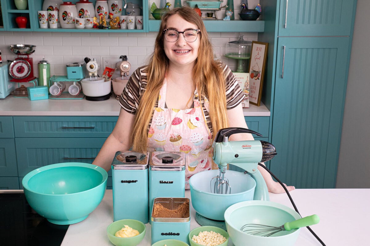 white chocolate chip macadamia nut cookies  ingredients in bowls on a kitchen counter with a girl smiling wearing an apron.