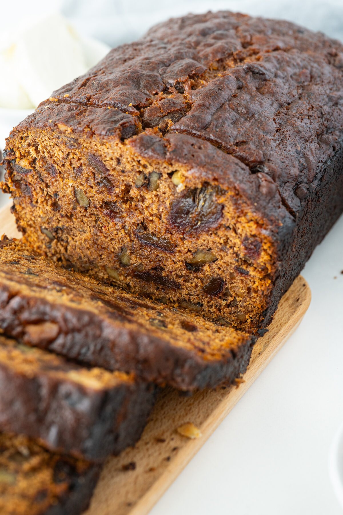 A close-up of a sliced loaf of dark fruitcake with visible pieces of nuts and dried fruit, resting on a wooden cutting board.