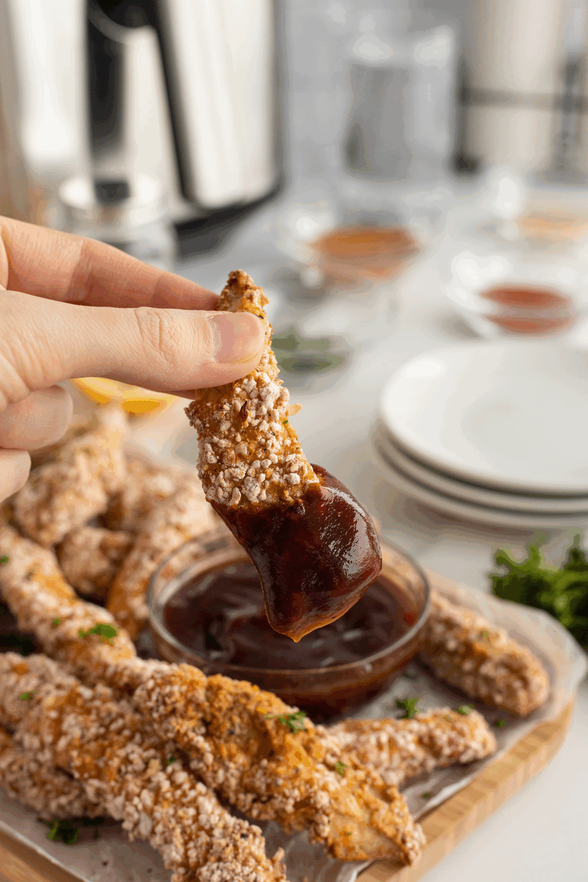 A hand holding a piece of fried chicken with sauce.
