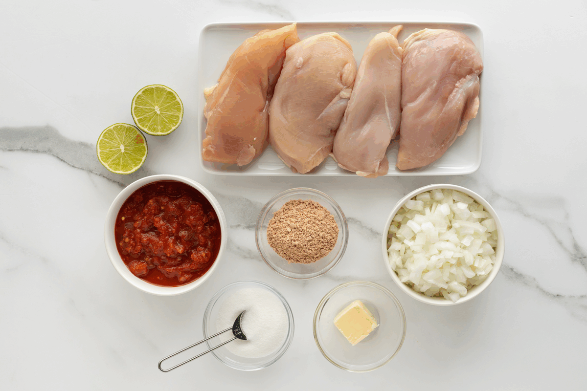 Ingredients laid out on a white surface: four raw chicken breasts, two lime halves, a bowl of chopped onions, a bowl of salsa, a bowl of breadcrumbs, a small bowl of sugar, and a small dish of butter with a spoon.
