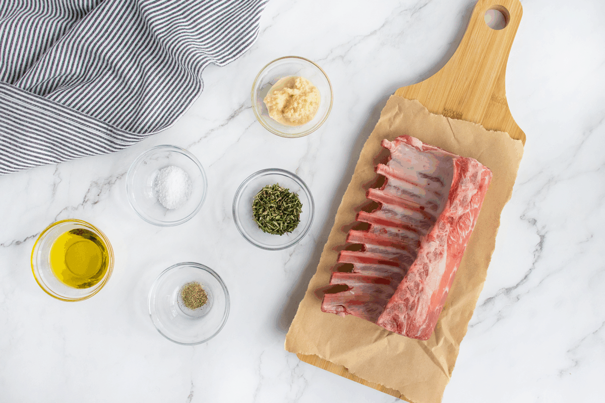 A rack of ribs on a cutting board next to bowls of spices.