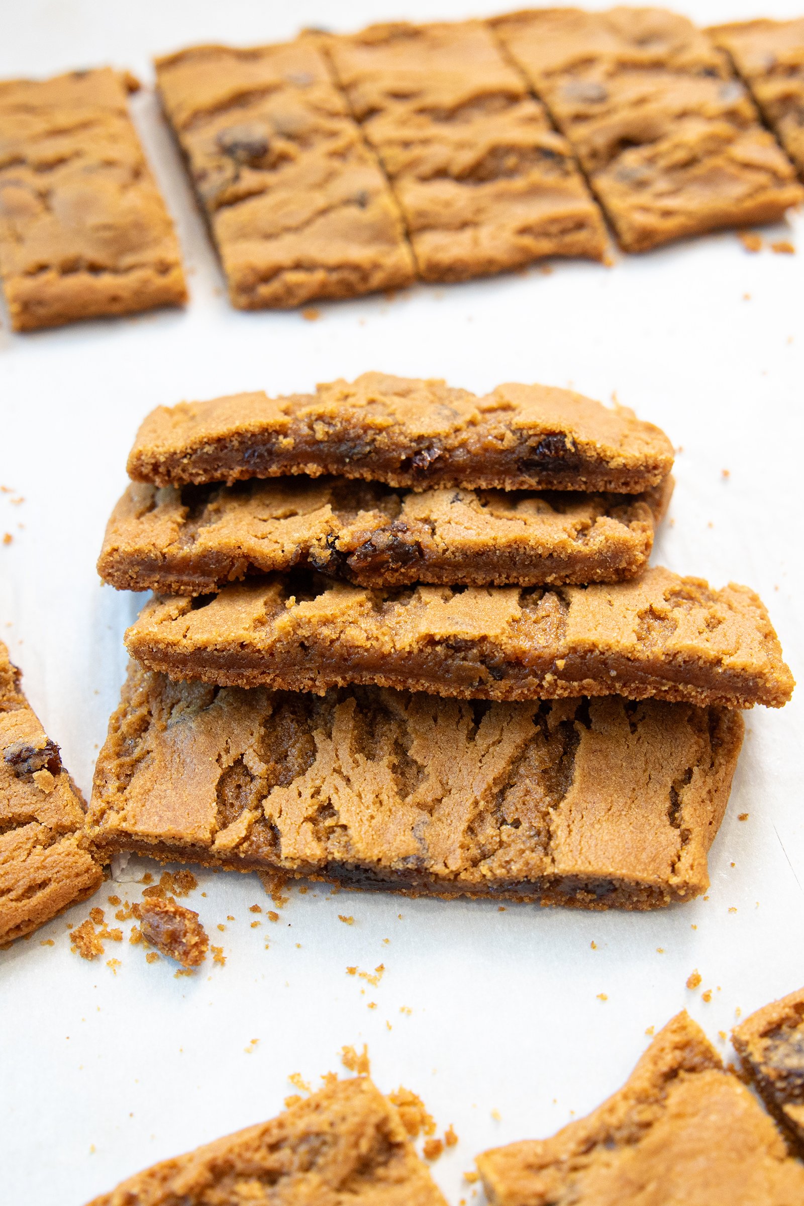 Several rectangular cookie bars are stacked and scattered on a white surface. The bars are golden brown with visible chocolate chunks and a soft, chewy texture.