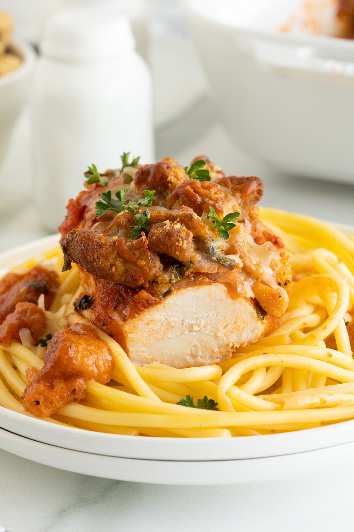A plate of spaghetti topped with a sliced, breaded chicken breast, marinara sauce, melted cheese, and garnished with fresh parsley.